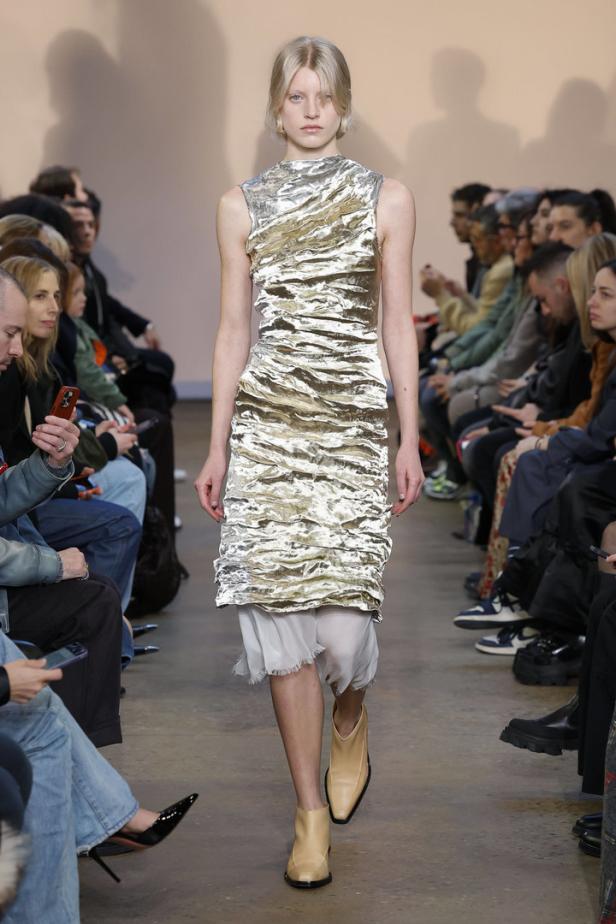 Ein Model präsentiert ein ärmelloses, gerafftes Kleid auf dem Laufsteg.