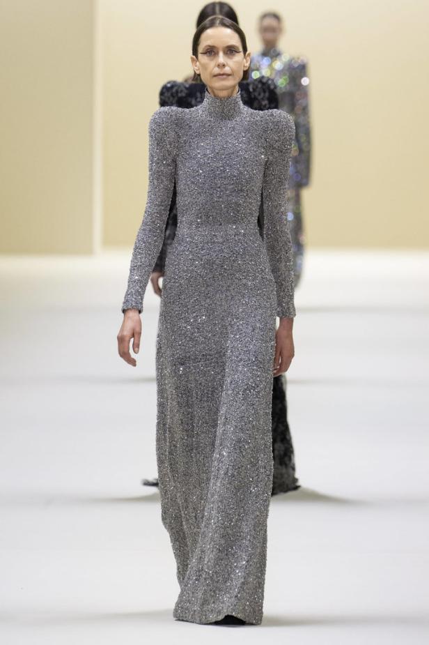 Ein Model präsentiert ein silbernes, glitzerndes Abendkleid auf dem Laufsteg.