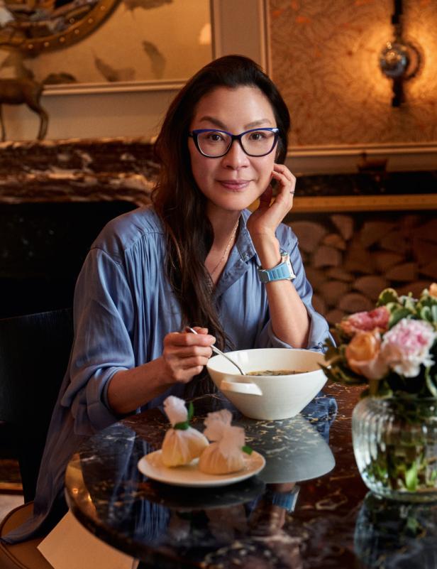 Michelle Yeoh sitzt an einem Tisch und isst Suppe.