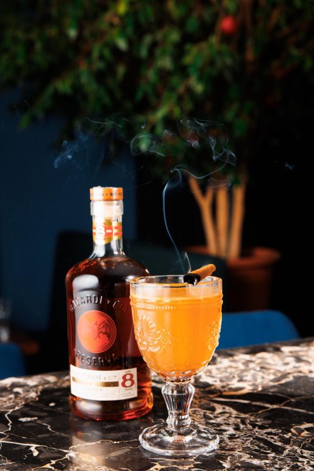 Ein Glas Hot Buttered Rum mit einer Zimtstange und einer Flasche Bacardi Rum auf einem Tisch.