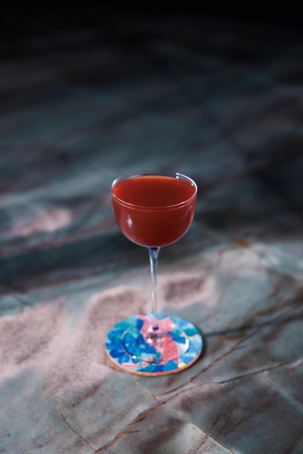 Ein roter Cocktail in einem eleganten Glas steht auf einem farbenfrohen Untersetzer.