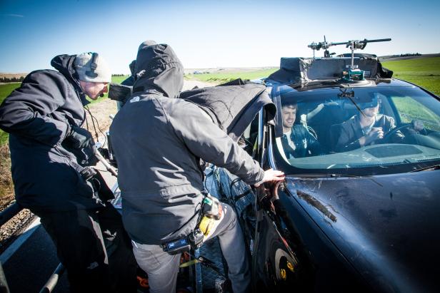 Ein Filmteam dreht eine Szene mit zwei Schauspielern in einem Auto.