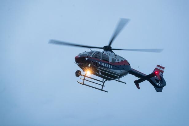Ein Polizeihubschrauber mit eingeschaltetem Suchscheinwerfer fliegt am Himmel.