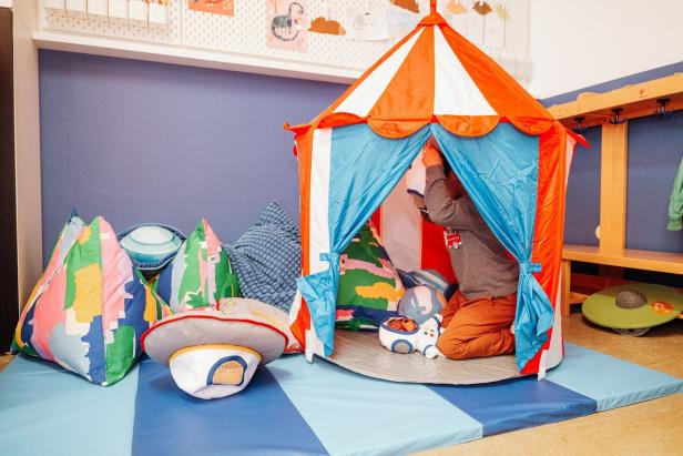 Ein Kind spielt in einem Zirkuszelt, umgeben von Kissen und Spielzeug.