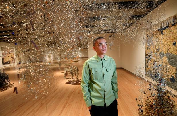 Ein Mann steht in einer Kunstgalerie vor einer Installation aus Draht und Perlen.
