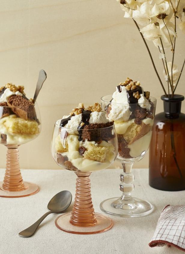 Drei Dessertgläser gefüllt mit Kuchen, Pudding, Sahne, Schokoladensoße und Walnüssen.