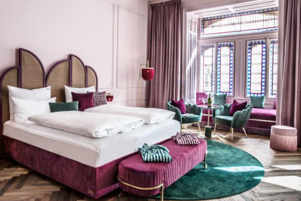 Ein Schlafzimmer in Rosa- und Lilatönen mit einem Doppelbett und einem Fenster mit Buntglas.
