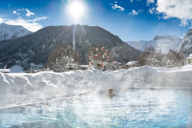 Eine Frau schwimmt in einem Außenpool mit Blick auf eine verschneite Berglandschaft.