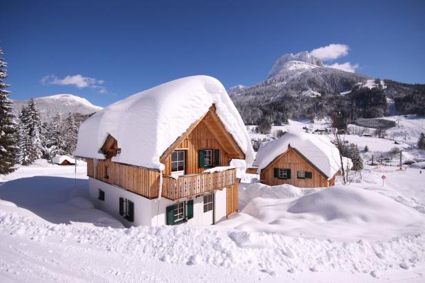 Ein Holzhaus mit grünen Fensterläden ist im Winter mit Schnee bedeckt.