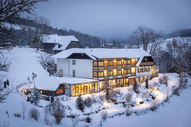 Ein verschneites Hotel in einer winterlichen Landschaft mit beleuchteten Fenstern.