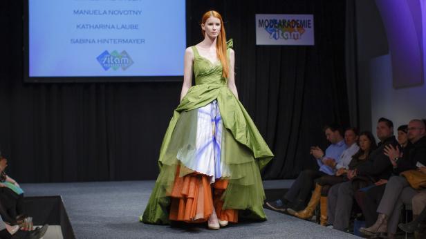 Eine rothaarige Frau präsentiert ein grünes Kleid auf dem Laufsteg einer Modenschau.