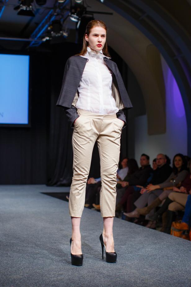 Eine Frau präsentiert ein Outfit mit Bluse, Hose und Blazer auf einem Laufsteg.