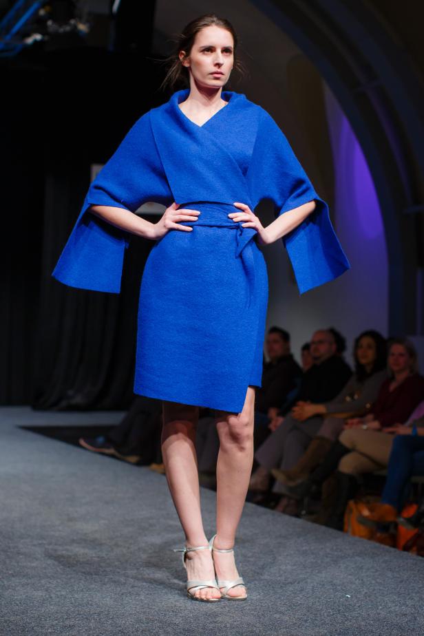 Eine Frau präsentiert ein blaues Kleid mit weiten Ärmeln auf einem Laufsteg.