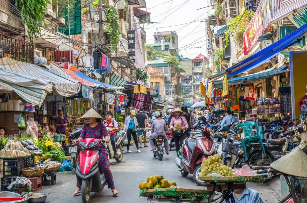 Eine belebte Straße in Hanoi, Vietnam, mit Händlern, Mopeds und Fußgängern.