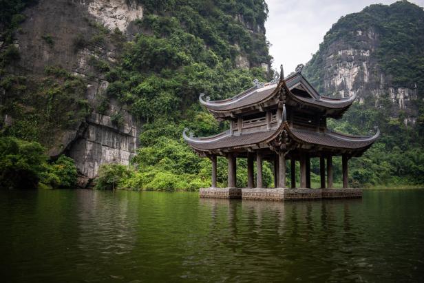 Ein Pavillon steht im Wasser, umgeben von grünen Bergen.