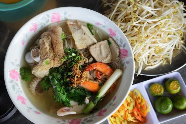 Eine Schüssel vietnamesische Nudelsuppe mit Schweinefuß, Garnelen und Tofu, serviert mit Limetten und Sprossen.