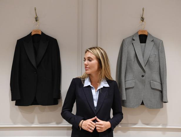 Eine Frau in einem Anzug steht zwischen einem schwarzen und einem grau gemusterten Blazer.