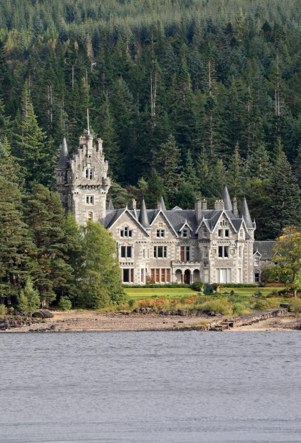 Das Balmoral Castle in Schottland liegt am Ufer eines Sees, umgeben von dichten Wäldern.