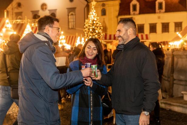 Drei Personen stoßen auf einem Weihnachtsmarkt mit Glühwein an.