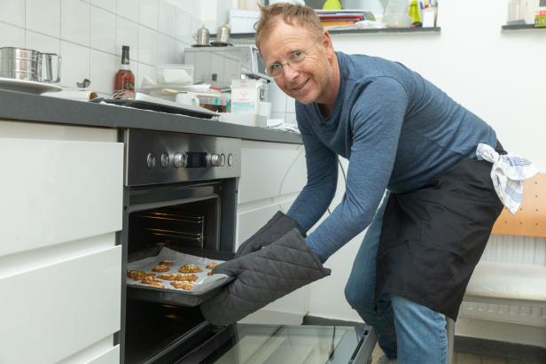 Ein Mann mit Ofenhandschuhen holt ein Backblech mit Keksen aus dem Ofen.