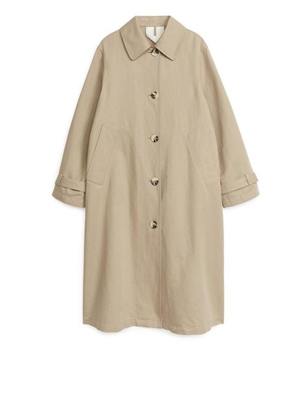 Ein beigefarbener Trenchcoat mit Knöpfen vor einem weißen Hintergrund.