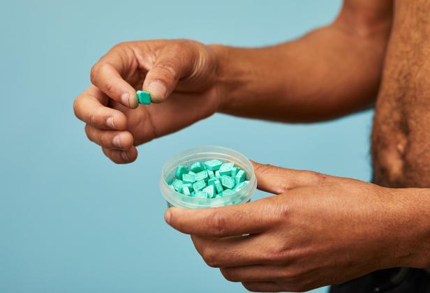 Eine Person hält eine Dose mit türkisfarbenen, quadratischen Bonbons.