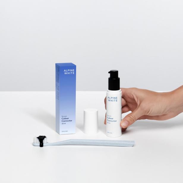 Eine Hand hält eine Flasche Alpine White Serum Colour Corrector neben einer Zahnbürste mit schwarzer Zahnpasta.