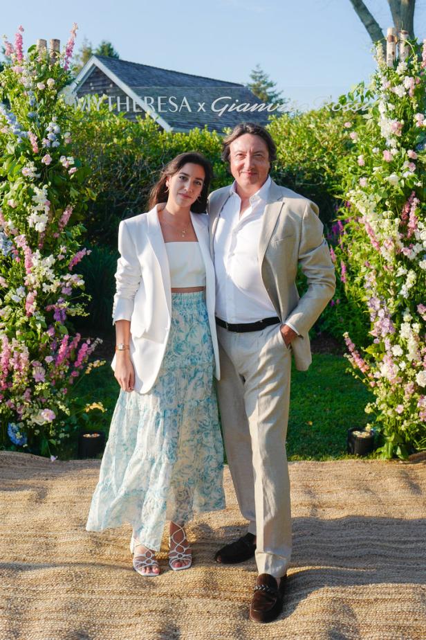Eine Frau und ein Mann posieren vor einem Blumengesteck mit der Aufschrift „Mytheresa x Gianvito Rossi“.