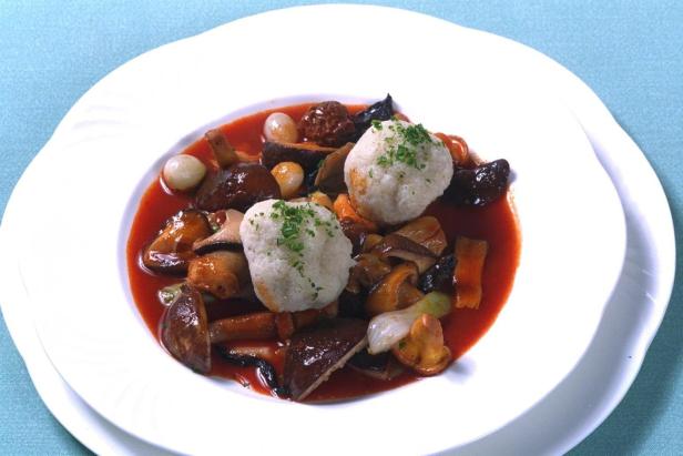 Ein Teller mit Pilzragout und zwei Serviettenknödeln in Sauce.