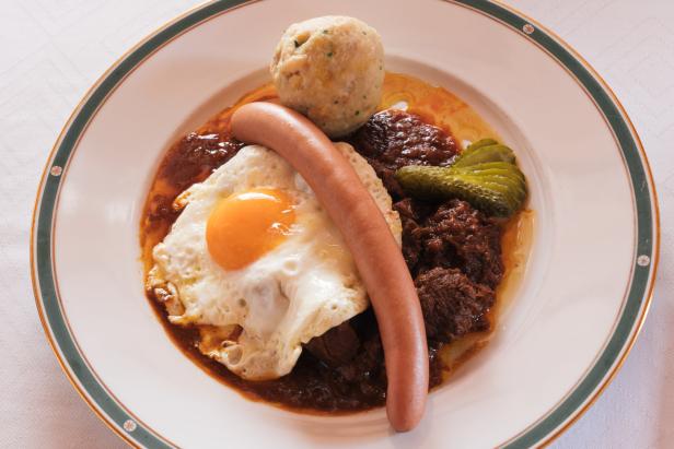 Ein Teller mit Rindfleisch, Spiegelei, Knödel, Wurst und Gurken.