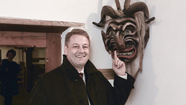 Ein Mann zeigt auf eine Krampusmaske an der Wand.