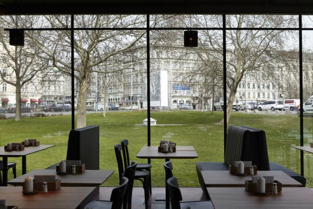 Blick aus einem Restaurant auf eine Grünfläche mit Bäumen und Stadtverkehr.