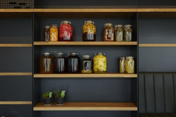 Regale mit großen Gläsern eingelegtem Obst und Gemüse sowie zwei kleinen Topfpflanzen.