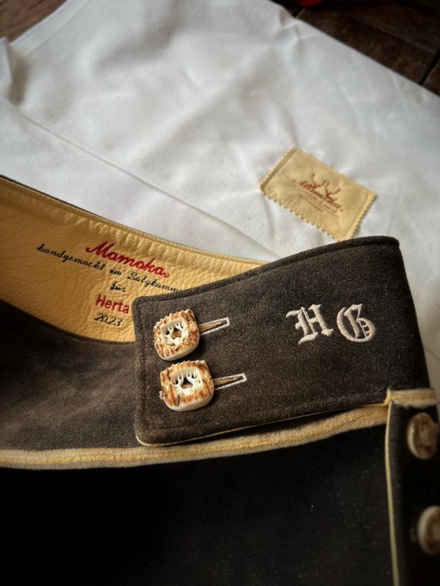 Detailaufnahme einer braunen Lederhose mit Knöpfen aus Hirschhorn und der Initiale „HG“.