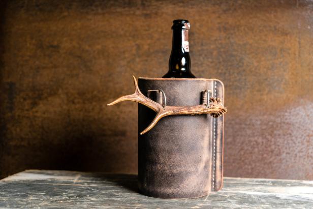 Eine Bierflasche in einem Lederbecher mit Geweihverzierung.