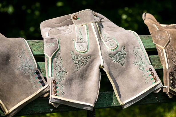 Lederhosen mit grünen Stickereien liegen auf einer grünen Bank.