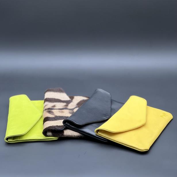 Vier verschiedene Handtaschen in Gelb, Schwarz und mit Zebramuster liegen auf einem dunklen Untergrund.