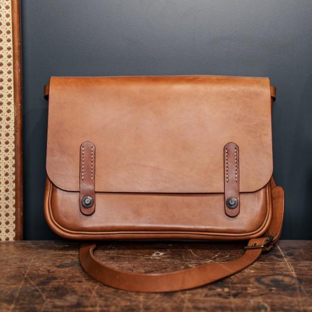 Eine hellbraune Ledertasche steht auf einem Holztisch.