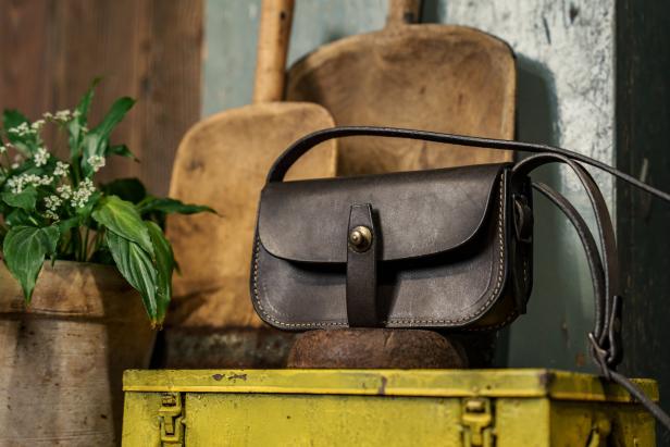 Eine schwarze Ledertasche steht auf einer gelben Kiste, neben einer Topfpflanze.