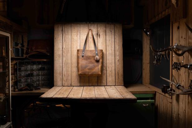 Eine braune Ledertasche hängt an einer Holzwand in einem rustikalen Raum.