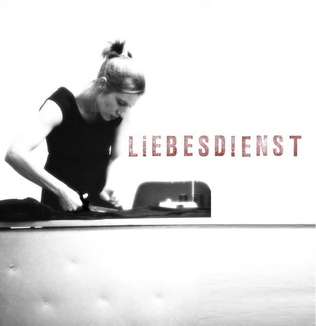 Eine Frau schneidet Stoff mit einer Schere, im Hintergrund der Schriftzug „Liebesdienst“.