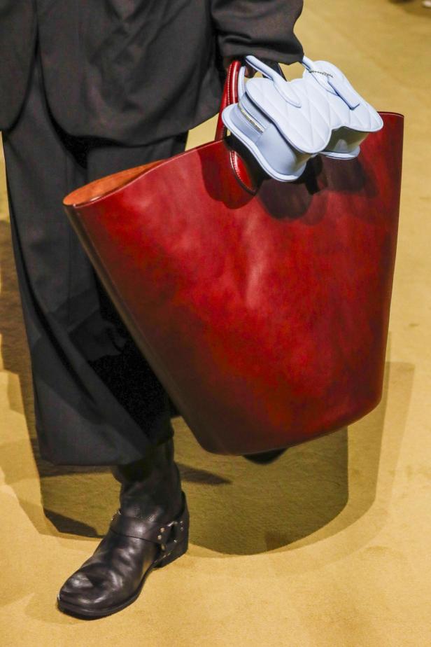 Eine Person trägt eine rote Tragetasche und eine hellblaue, herzförmige Handtasche von Coach.