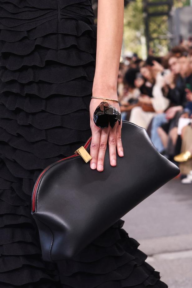 Eine Hand mit einem auffälligen Ring hält eine schwarze Chloé-Handtasche.
