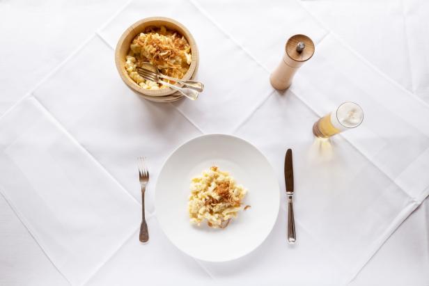 Käsespätzle mit Röstzwiebeln auf einem weißen Teller, dazu ein Bier und eine Pfeffermühle.