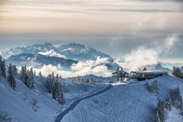 Winterlandschaft mit schneebedeckten Bergen und einem modernen Gebäude auf einem Hügel.