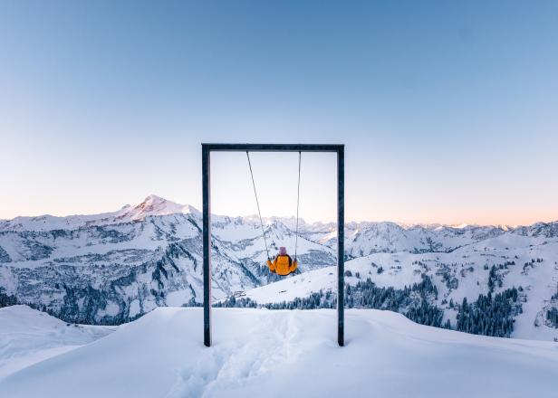 Eine Person schaukelt auf einer Schaukel mit Blick auf eine verschneite Berglandschaft.
