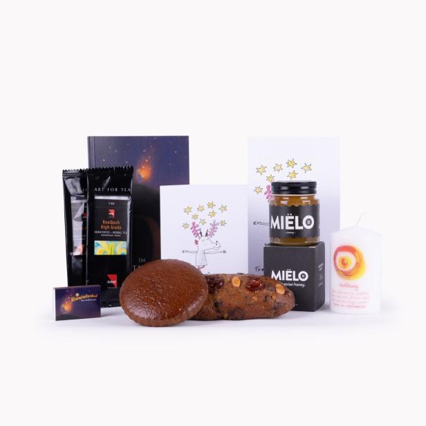 Ein Arrangement mit Tee, Honig von Mielo, Gebäck, einer Kerze und einer Karte von Sterntalerhof.