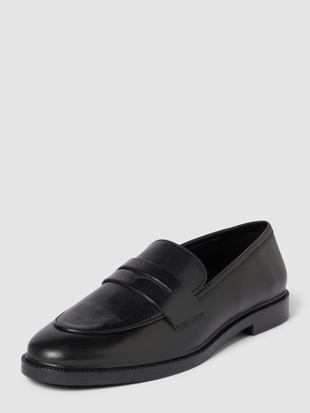 Ein schwarzer Pennyloafer aus Leder steht auf einem hellgrauen Hintergrund.