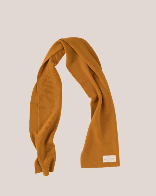 Ein ockerfarbener Strickschal ist vor einem neutralen Hintergrund drapiert.