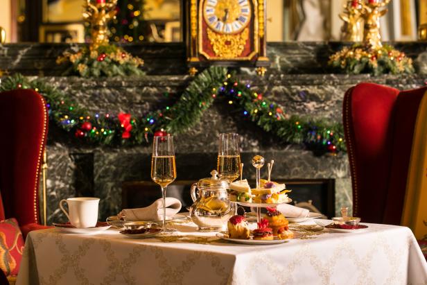 Ein festlich gedeckter Tisch mit Champagner, Gebäck und Sandwiches vor einem dekorierten Kamin.
